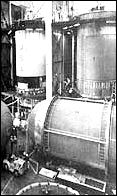 Production in full swing: in towers at right and center, stages are being checked before shipment to Sacramento for firing tests; in the left tower, a tank section is being cleaned before insulation is applied; in lower right, a tank is being given its final interior work and the completed tank at left is about to be hoisted into the tower from which the photos were taken